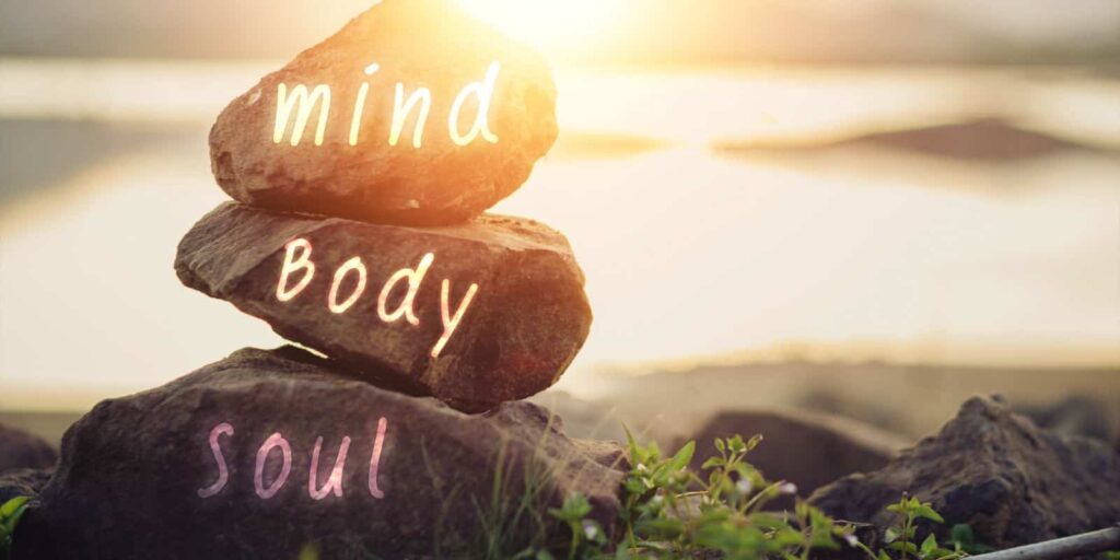 stacked rocks that say mind, body and soul on a beach