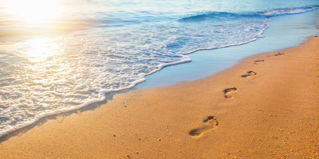 beach, wave and footprints at sunset time