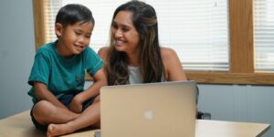 A Chaminade online undergraduate student works on her homework as her son looks at her laptop